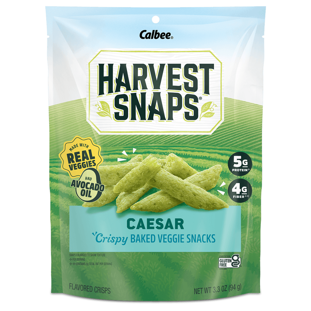 A 3.3 oz bag of Calbee Harvest Snaps Caesar crispy baked veggie snacks, featuring green chip illustrations on a light blue and green background.