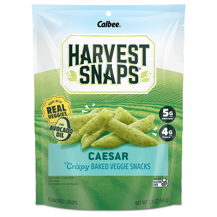 A 3.3 oz bag of Calbee Harvest Snaps Caesar crispy baked veggie snacks, featuring green chip illustrations on a light blue and green background.