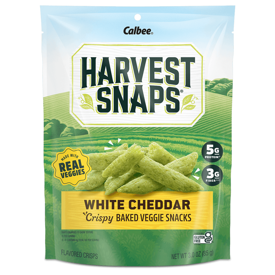Bag of Calbee Harvest Snaps, White Cheddar flavor. Features green fields background, "Made with Real Veggies" label, and protein, fiber info.