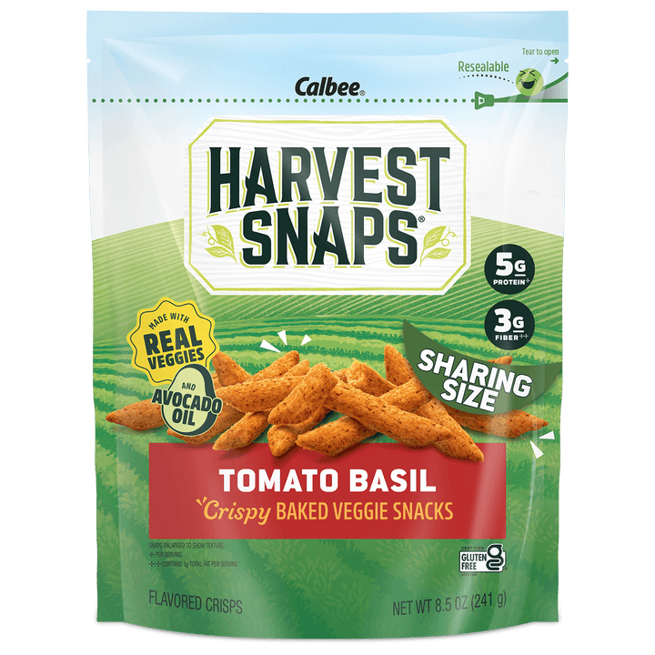 A bag of Calbee Harvest Snaps Tomato Basil crispy baked veggie snacks, shown against a plain white background. The packaging features a green and white design with an illustration of the golden-brown snack pieces.