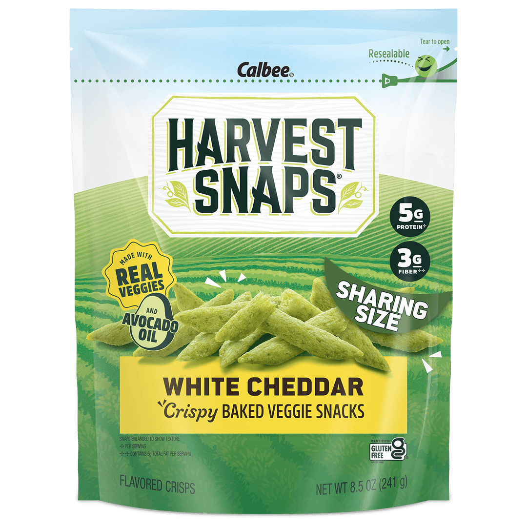 A package of Calbee Harvest Snaps White Cheddar Crispy Baked Veggie Snacks in a resealable stand-up pouch. The packaging is primarily green and white with a yellow banner at the bottom, showing images of the green veggie chips.