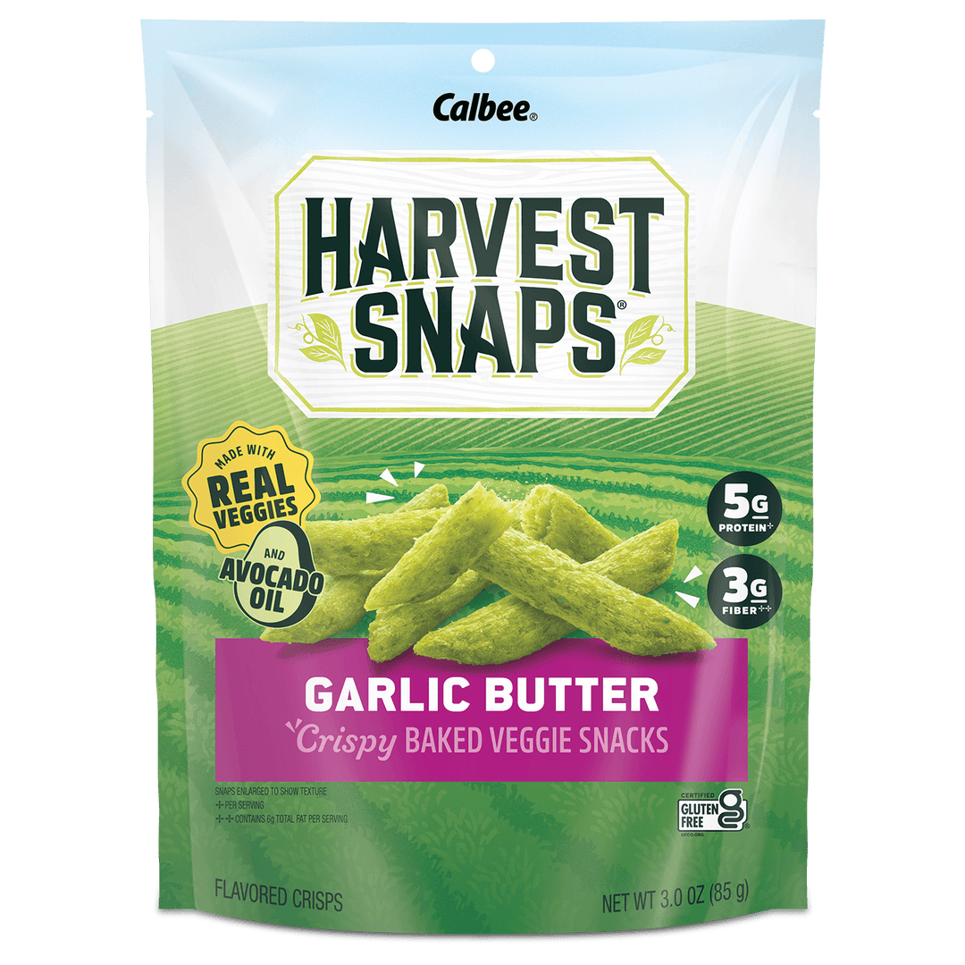 A 3 oz bag of Calbee Harvest Snaps Garlic Butter crispy baked veggie snacks. The packaging features a green field background with illustrations of the green snack sticks, a purple banner reading 'GARLIC BUTTER', and badges indicating 'Real Veggies' and 'Avocado Oil'.