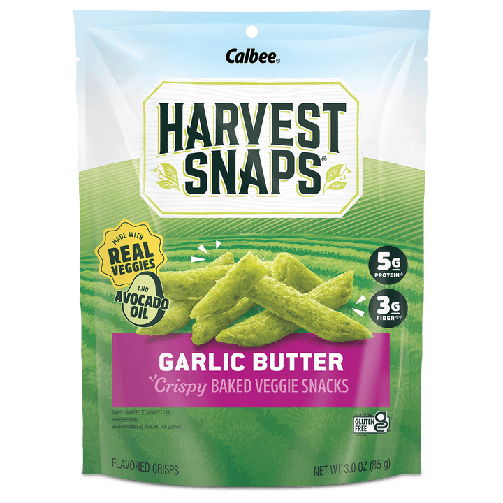 A 3 oz bag of Calbee Harvest Snaps Garlic Butter crispy baked veggie snacks. The packaging features a green field background with illustrations of the green snack sticks, a purple banner reading 'GARLIC BUTTER', and badges indicating 'Real Veggies' and 'Avocado Oil'.